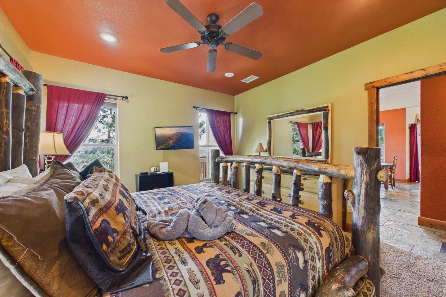 Bedroom featuring a log-frame bed with rustic patterned bedding, warm yellow walls, a terracotta-colored ceiling, and a ceiling fan.