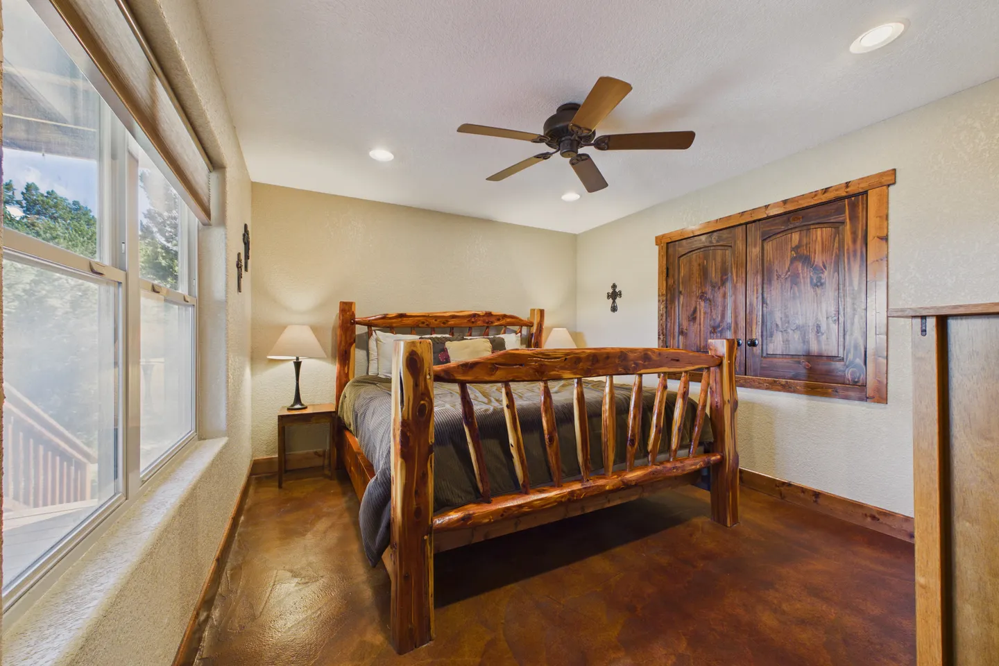 Bedroom featuring a log-style wooden bed frame, ceiling fan, stained concrete floor, and rustic wood-trimmed closet.