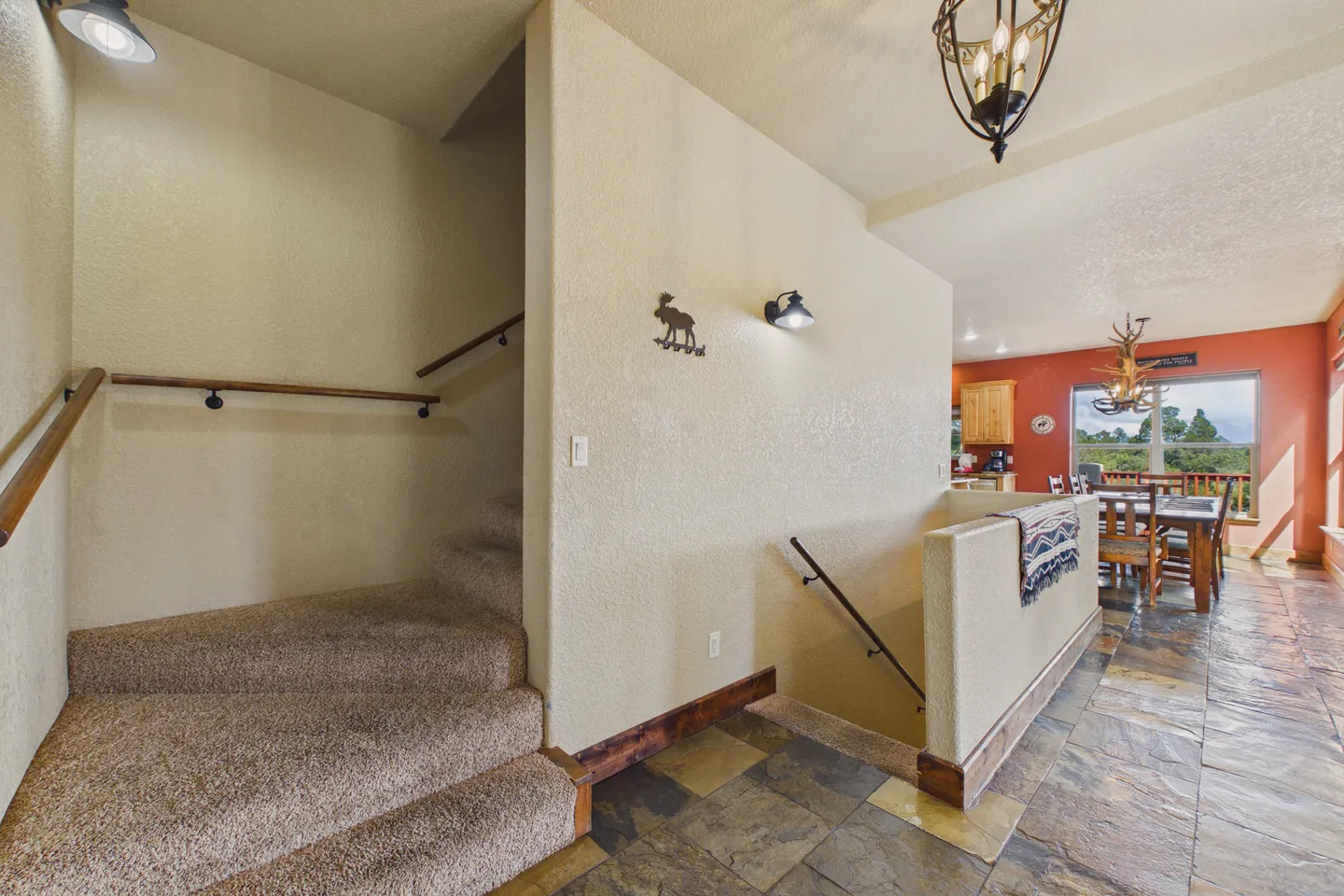 Stairways leading to upper and lower levels next to a stone-tiled hallway opening to a dining area.
