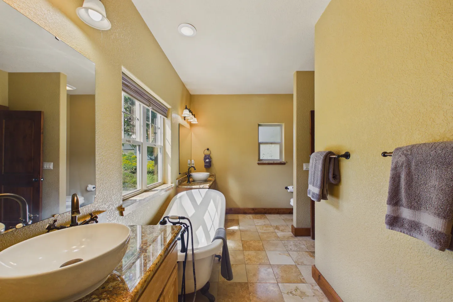 Bathroom featuring a freestanding clawfoot-style tub, vessel sinks on vanities, tiled floor, and soft yellow walls.