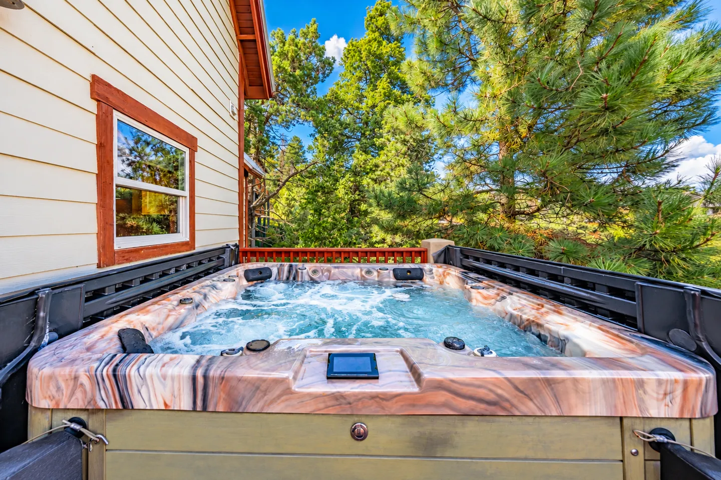 Outdoor hot tub filled with bubbling water on a deck surrounded by pine trees.