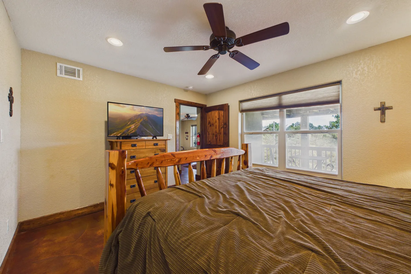 Bedroom featuring a log-style bed frame, a matching wooden dresser with a mounted television, a ceiling fan, and a window with blinds.