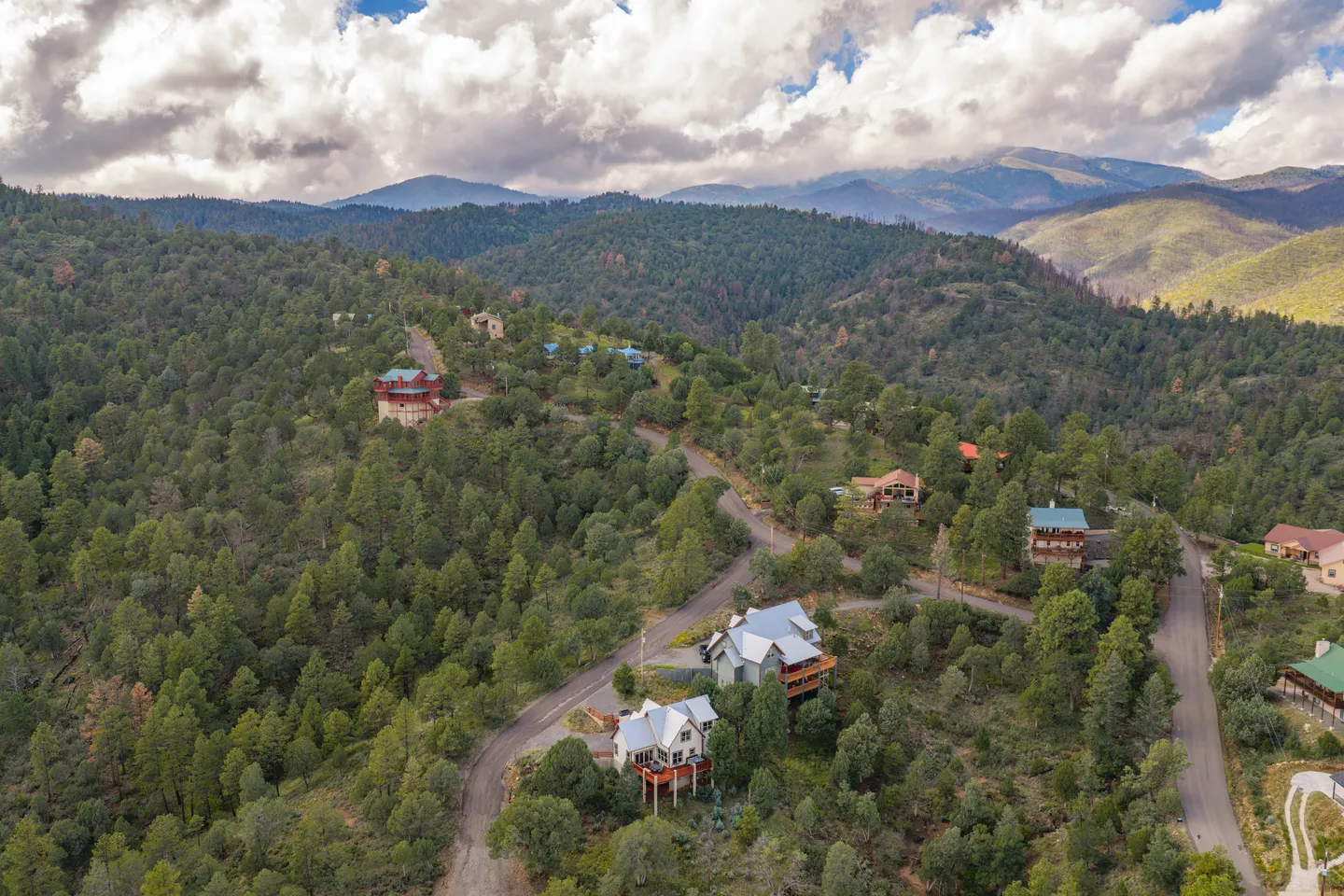 Aerial view of homes nestled along a winding road among forested hills and distant mountains.