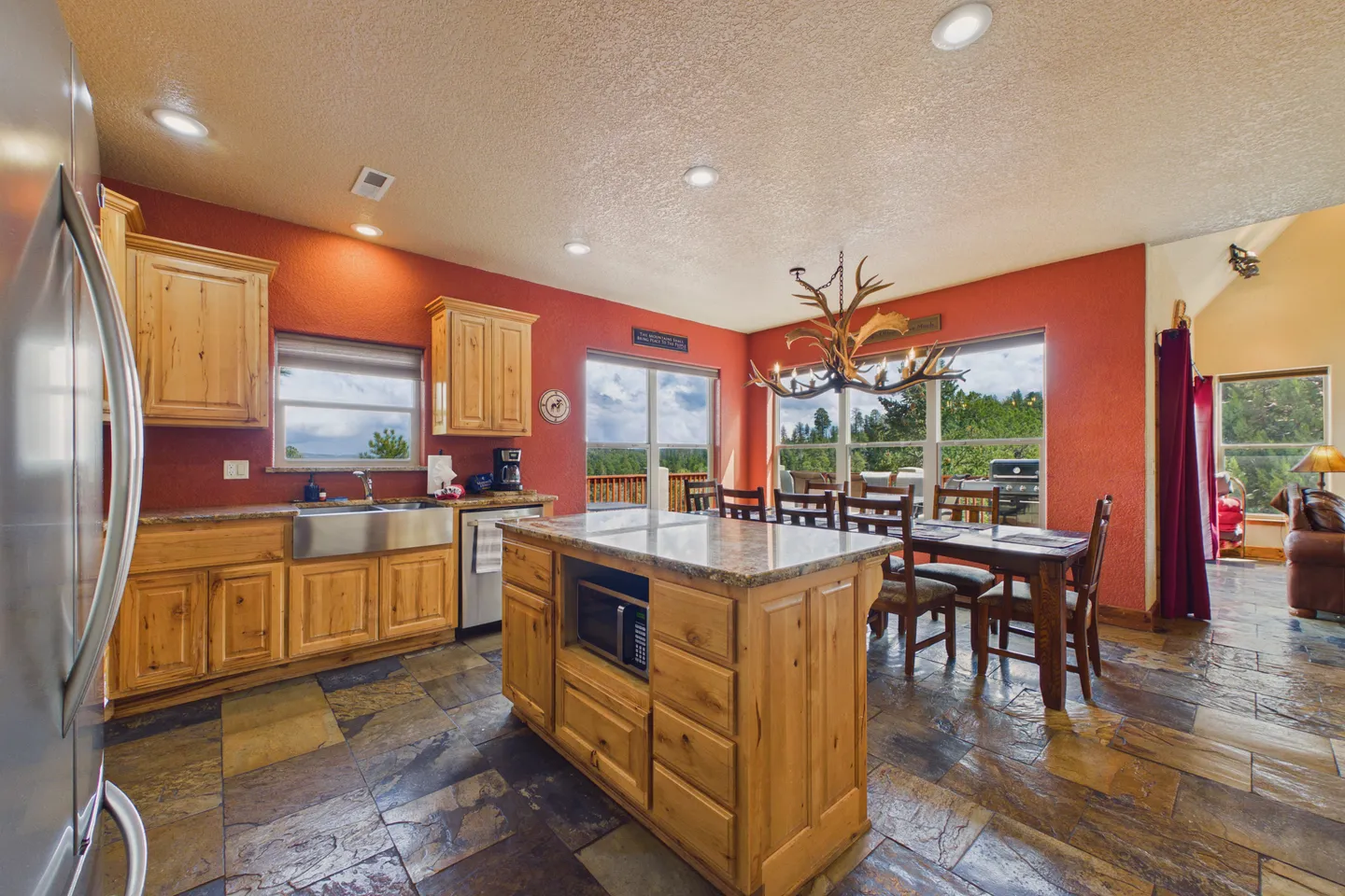 Open kitchen and dining area featuring terracotta walls, natural wood cabinets, a central island, and an antler chandelier above a dining table.