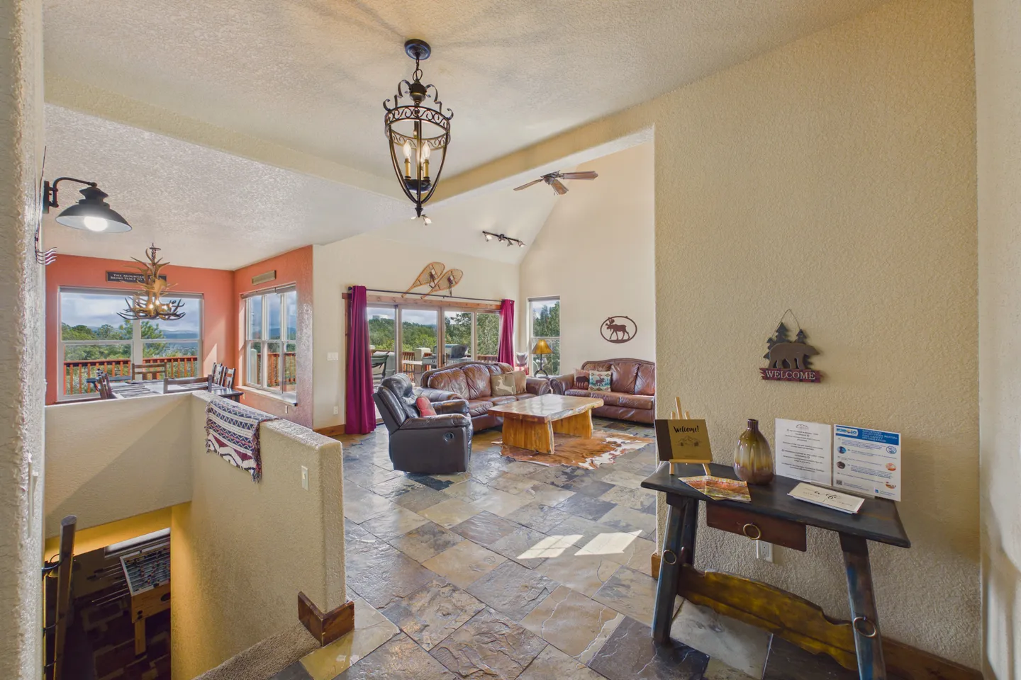 Open-concept living room and dining area with stone-look tile flooring, leather seating, and vaulted ceilings.
