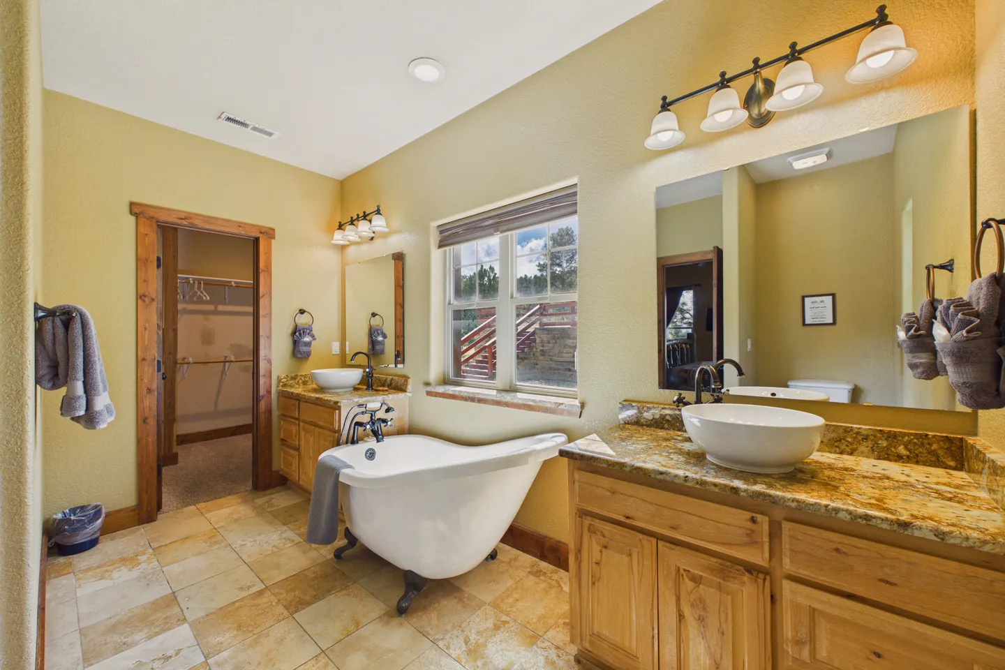 Bathroom with clawfoot soaking tub, dual separate vanities with vessel sinks, tile flooring, and view into walk-in closet.