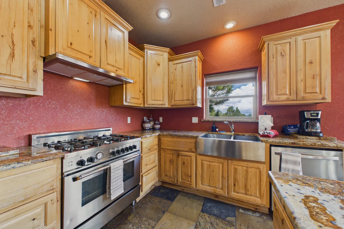 Kitchen corner featuring light wood knotty pine cabinets, terracotta red walls, a stainless steel range, and an apron-front stainless steel sink.