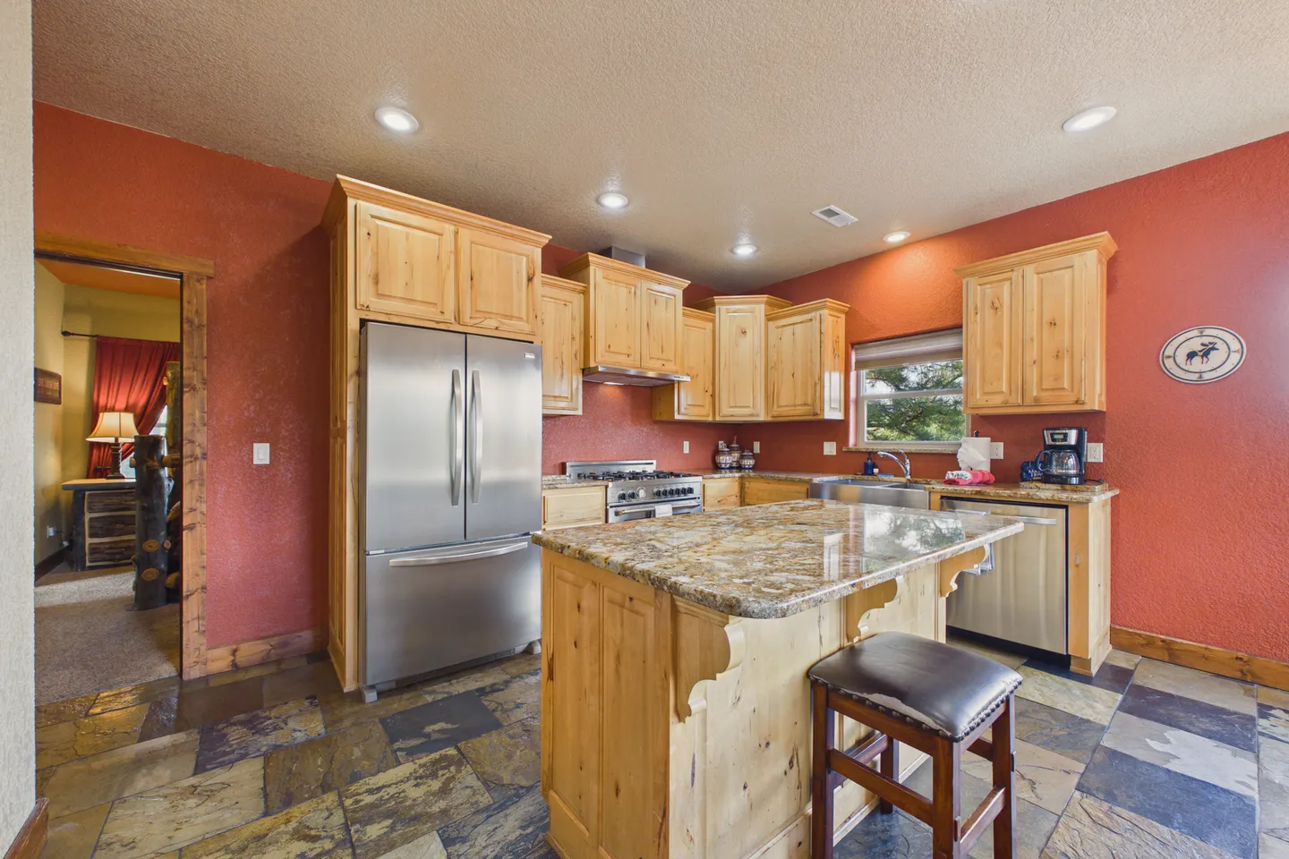 Kitchen with light wood cabinetry, red walls, stainless steel appliances, and a central island with a barstool.
