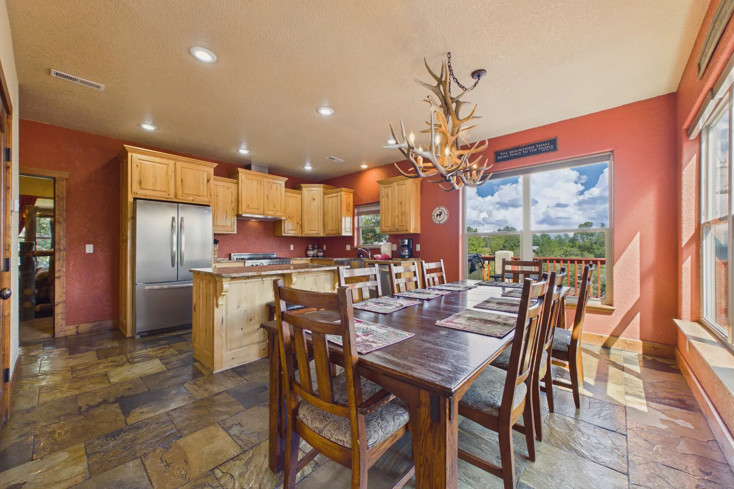 Dining area with a large wooden table, antler chandelier, and adjacent open kitchen with natural wood cabinets.