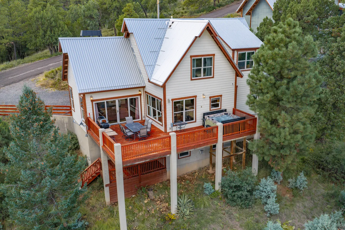 Elevated view of a multi-story house with a metal roof and an outdoor wooden deck featuring a dining table and hot tub.