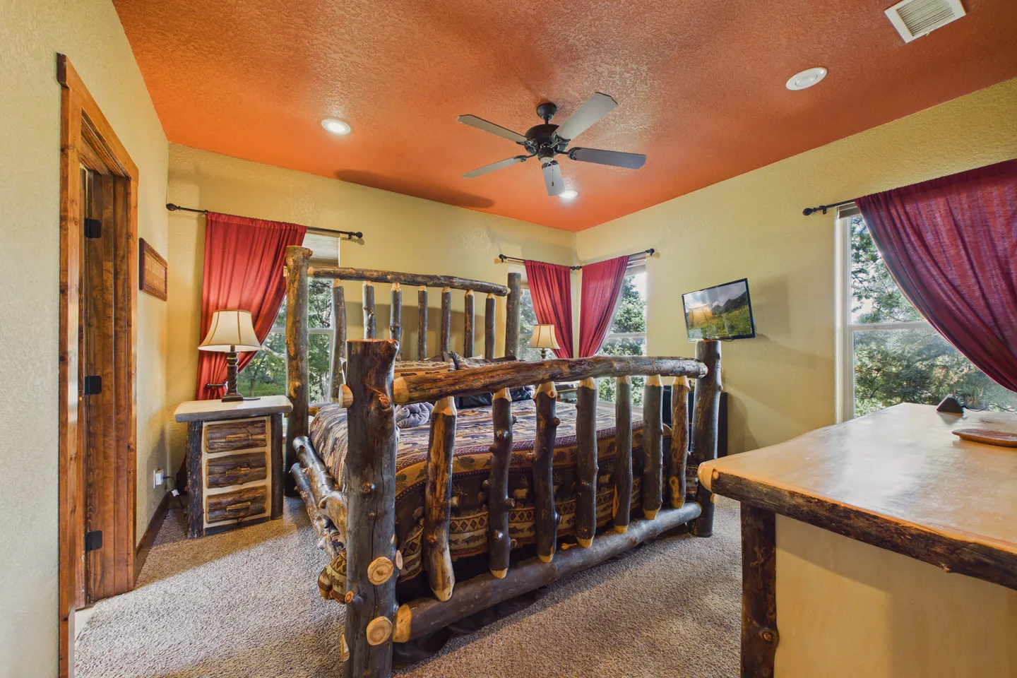 Bedroom featuring a natural log post bed, an orange painted ceiling with a ceiling fan, and red curtains on the windows.
