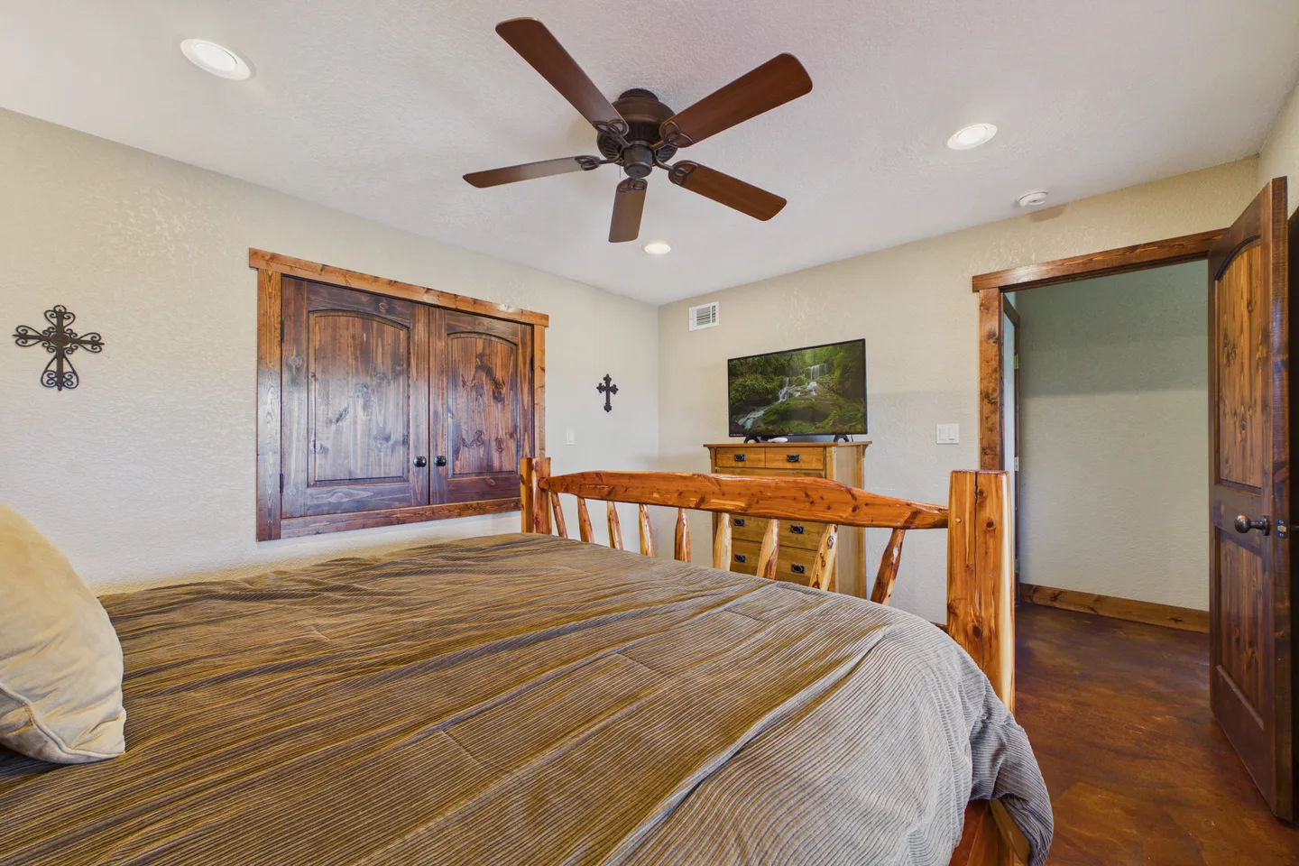 Bedroom featuring a log-style wooden bed, ceiling fan, wall-mounted wooden cabinet, and dresser with a television.