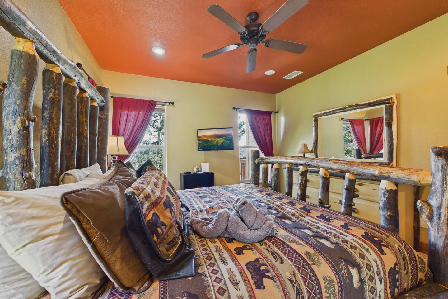 Bedroom featuring a log-style bed frame, rustic patterned quilt, orange ceiling with ceiling fan, and wall-mounted TV.