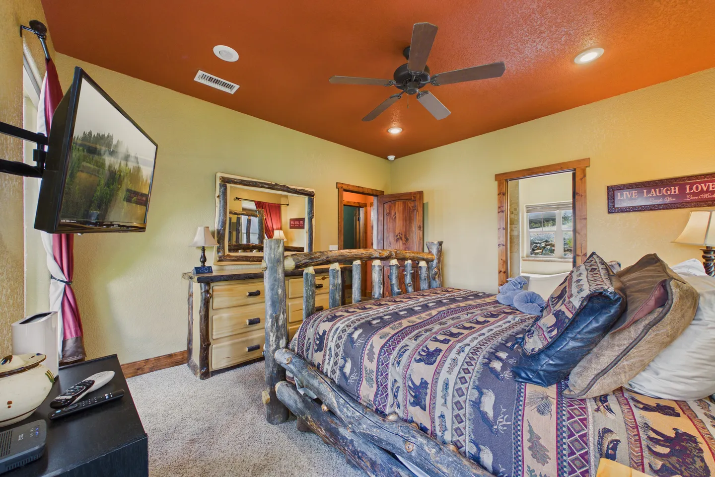 Bedroom featuring a natural log bed, rustic dresser, wall-mounted television, and a warm terracotta ceiling.