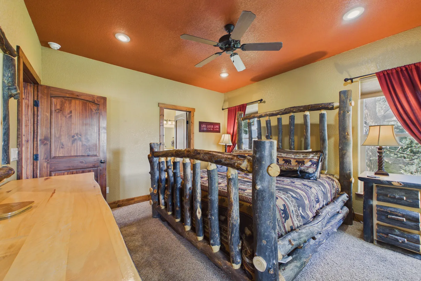 Rustic bedroom with a log-frame bed, matching nightstand, wooden dresser, and an orange ceiling.