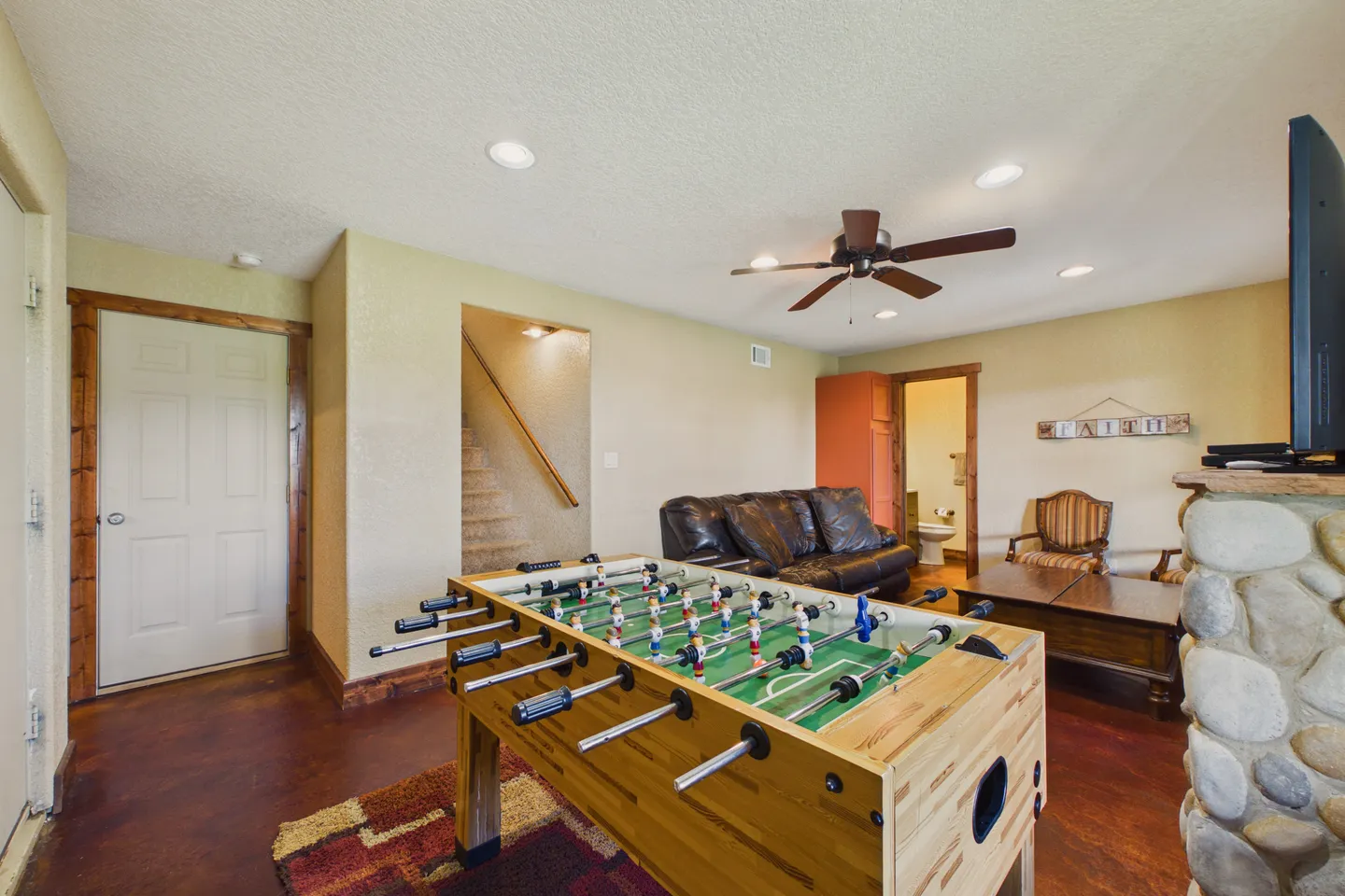 Game room featuring a wooden foosball table, a leather sofa, stairs, and a partial view of a stone fireplace.