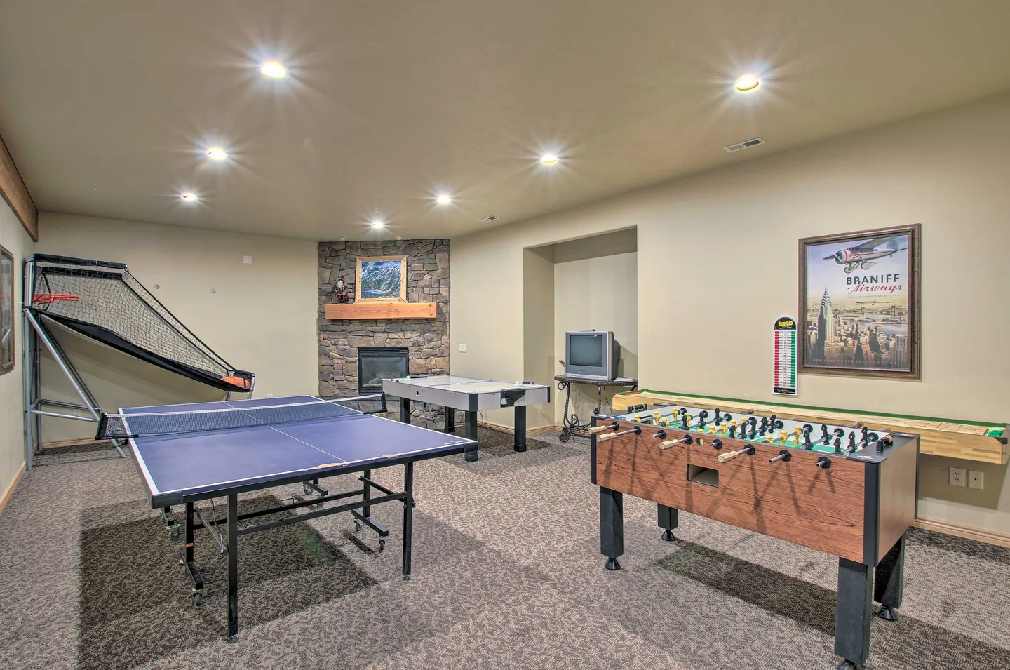 Game room featuring a ping-pong table, foosball table, air hockey table, basketball arcade game, and a corner stone fireplace.