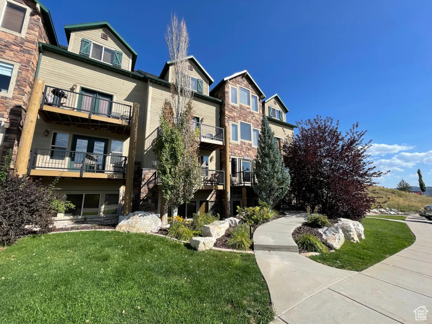 Exterior view of multi-story condominium building with stone accents, balconies, and a curved concrete walkway.