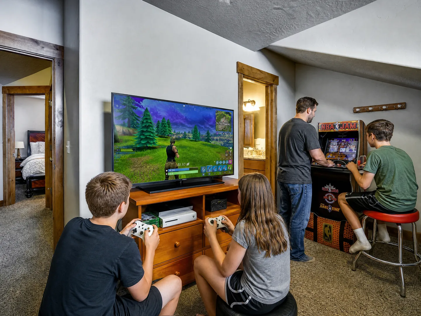 Game room area with people playing video games on a console hooked to a TV and an arcade cabinet.