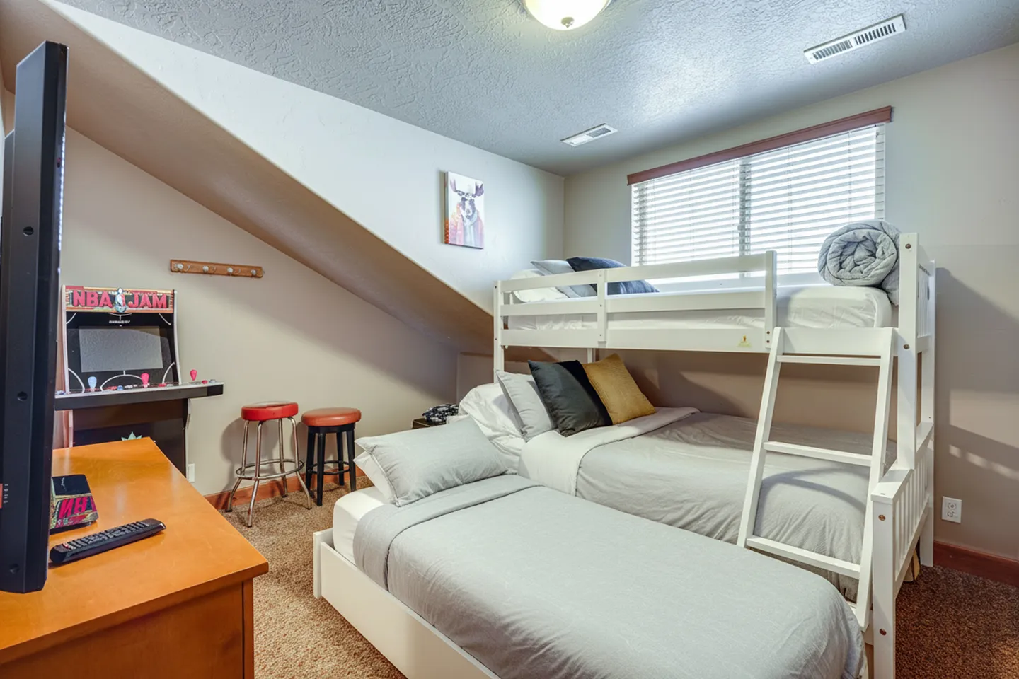 Bedroom with a white bunk bed, trundle-style single bed, television, and an NBA Jam arcade game cabinet.