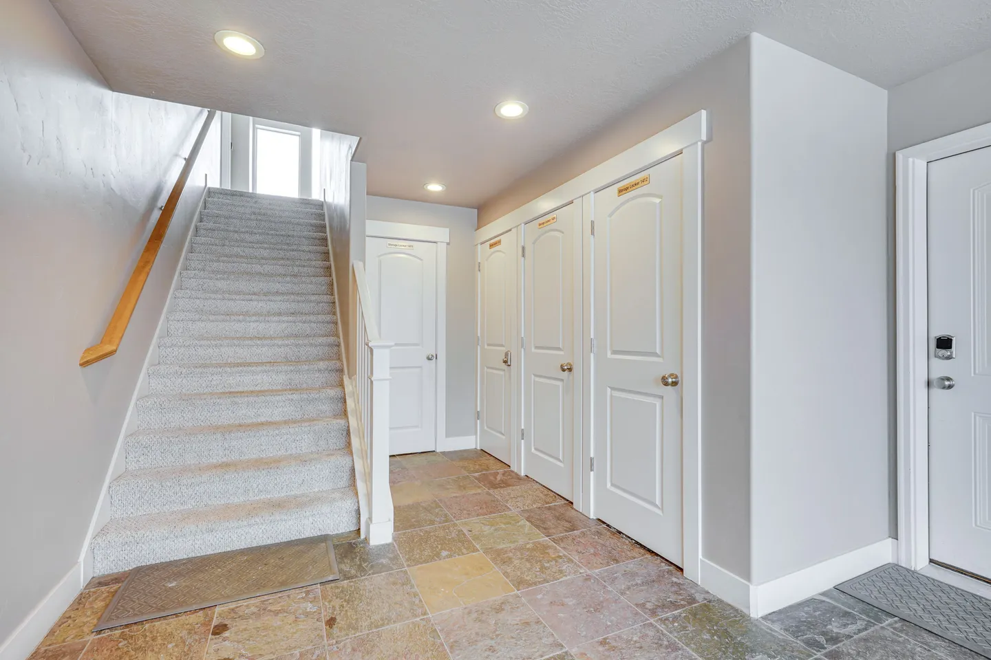Entryway hallway with tile flooring, a carpeted staircase leading up, and multiple white panel doors.