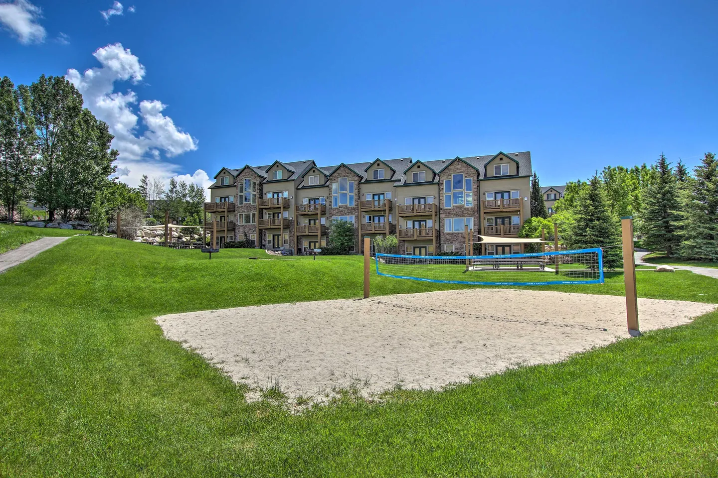 Outdoor sand volleyball court with a blue net on a green lawn in front of a multi-story residential building.