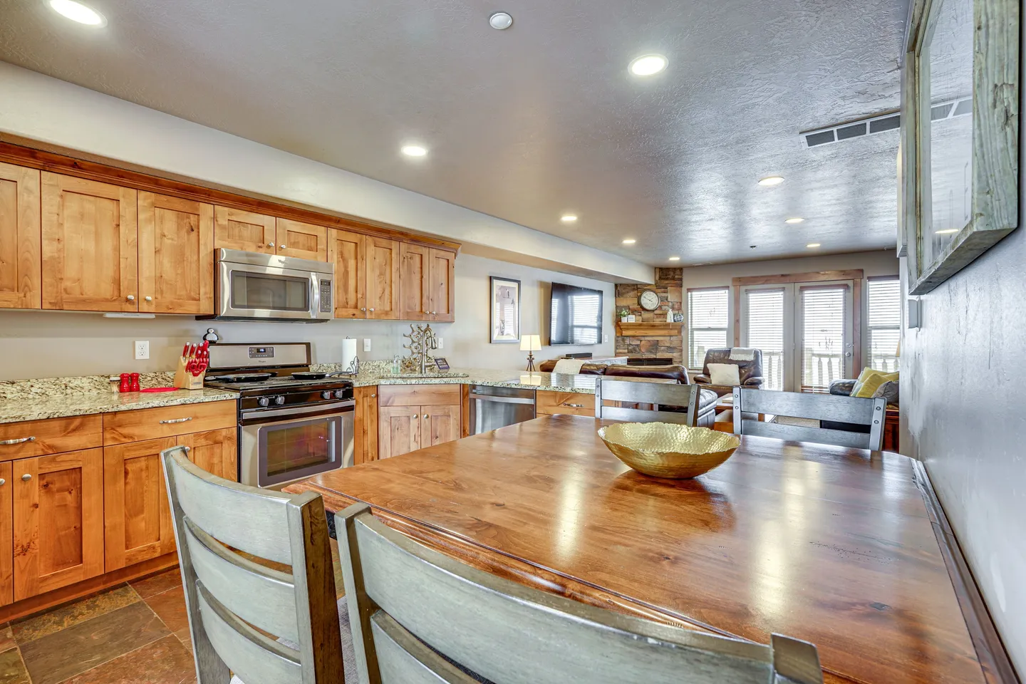 Open-concept dining area and kitchen with wooden table, light wood cabinetry, and a view into the living room.