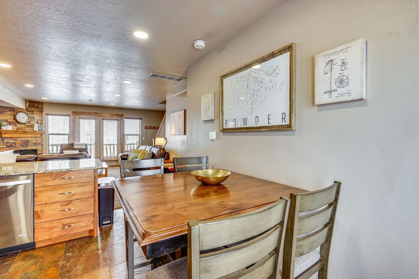 Dining area with a wooden table and slat-back chairs adjacent to a kitchen counter and living room.