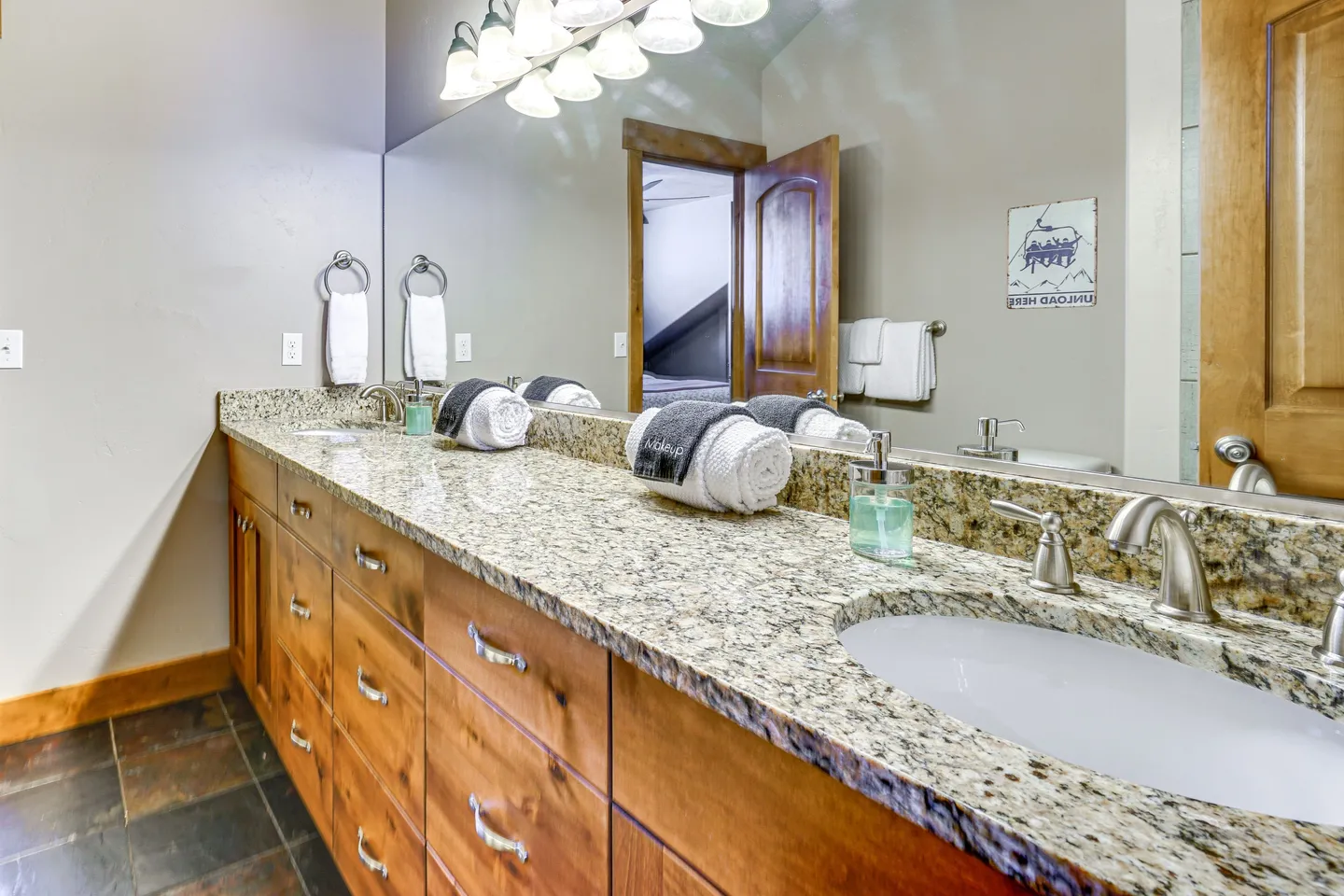 Bathroom vanity with dual undermount sinks, granite countertop, wooden drawers, and large mirror.