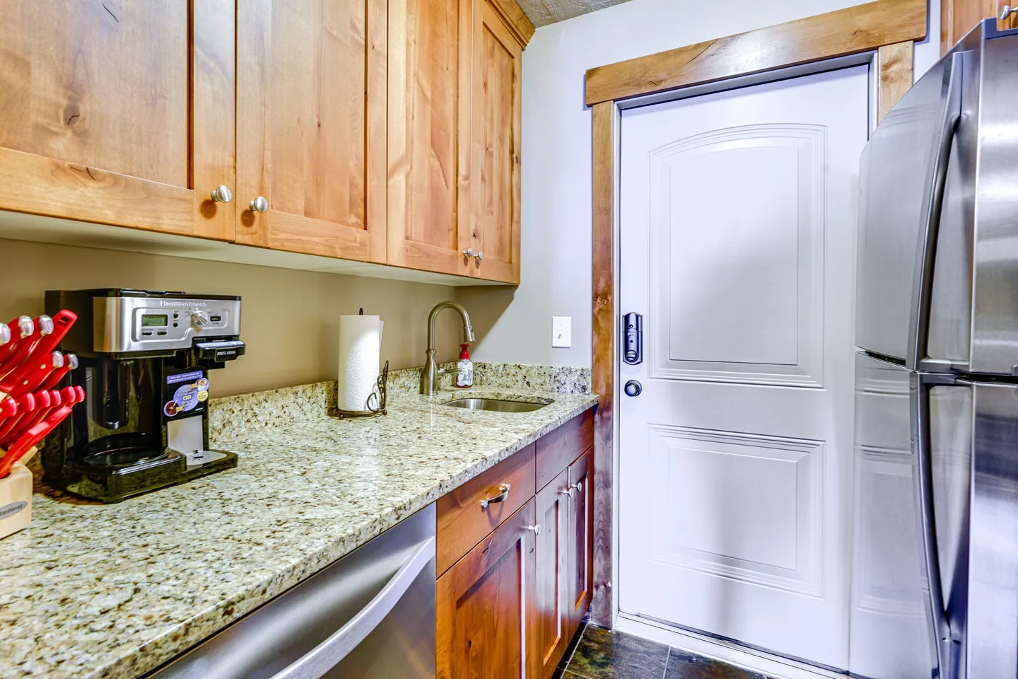 Kitchen counter area with wood cabinets, speckled granite countertops, a small sink, coffee maker, and an adjacent white door.