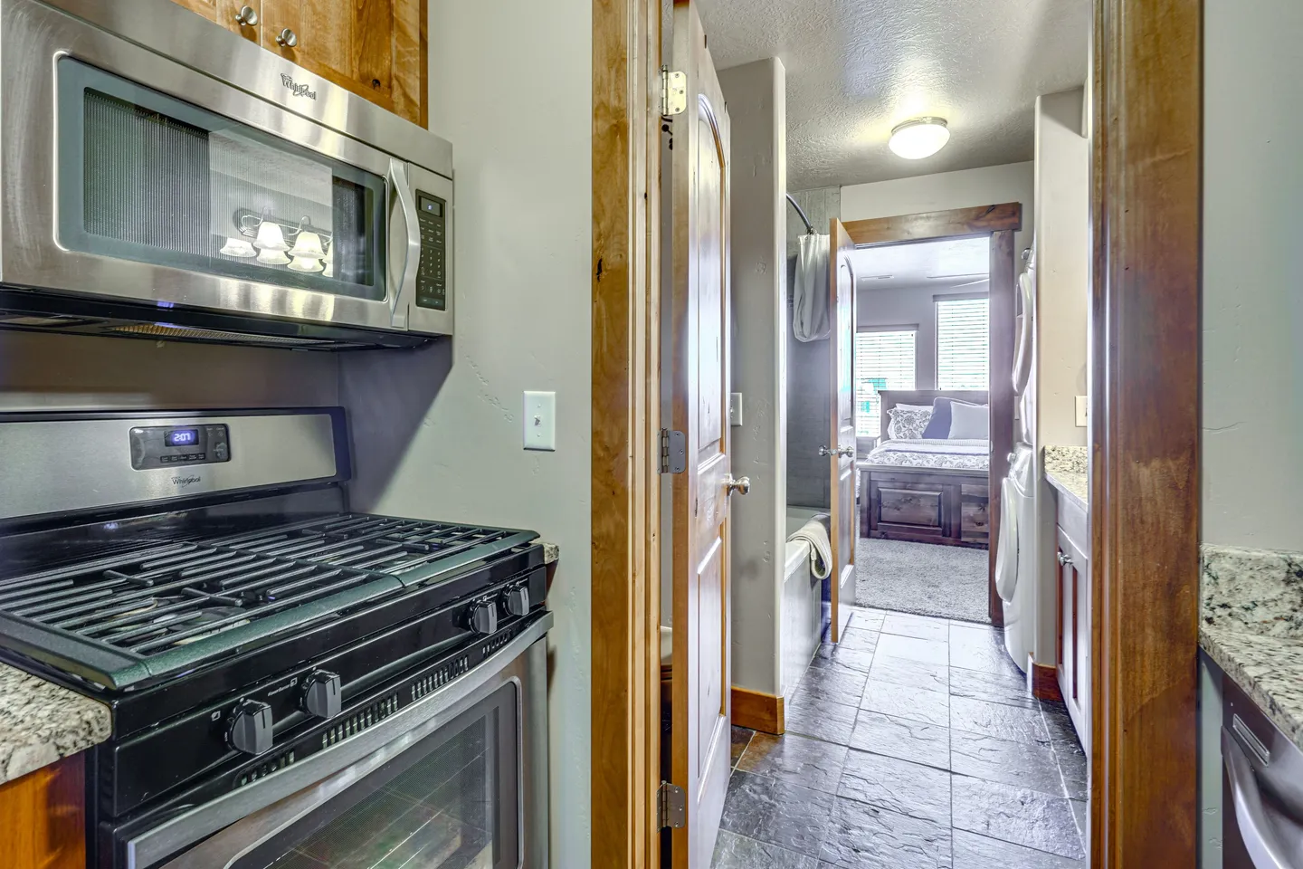 View from kitchen showing stainless steel microwave and stove looking through a hallway and bathroom into a bedroom.