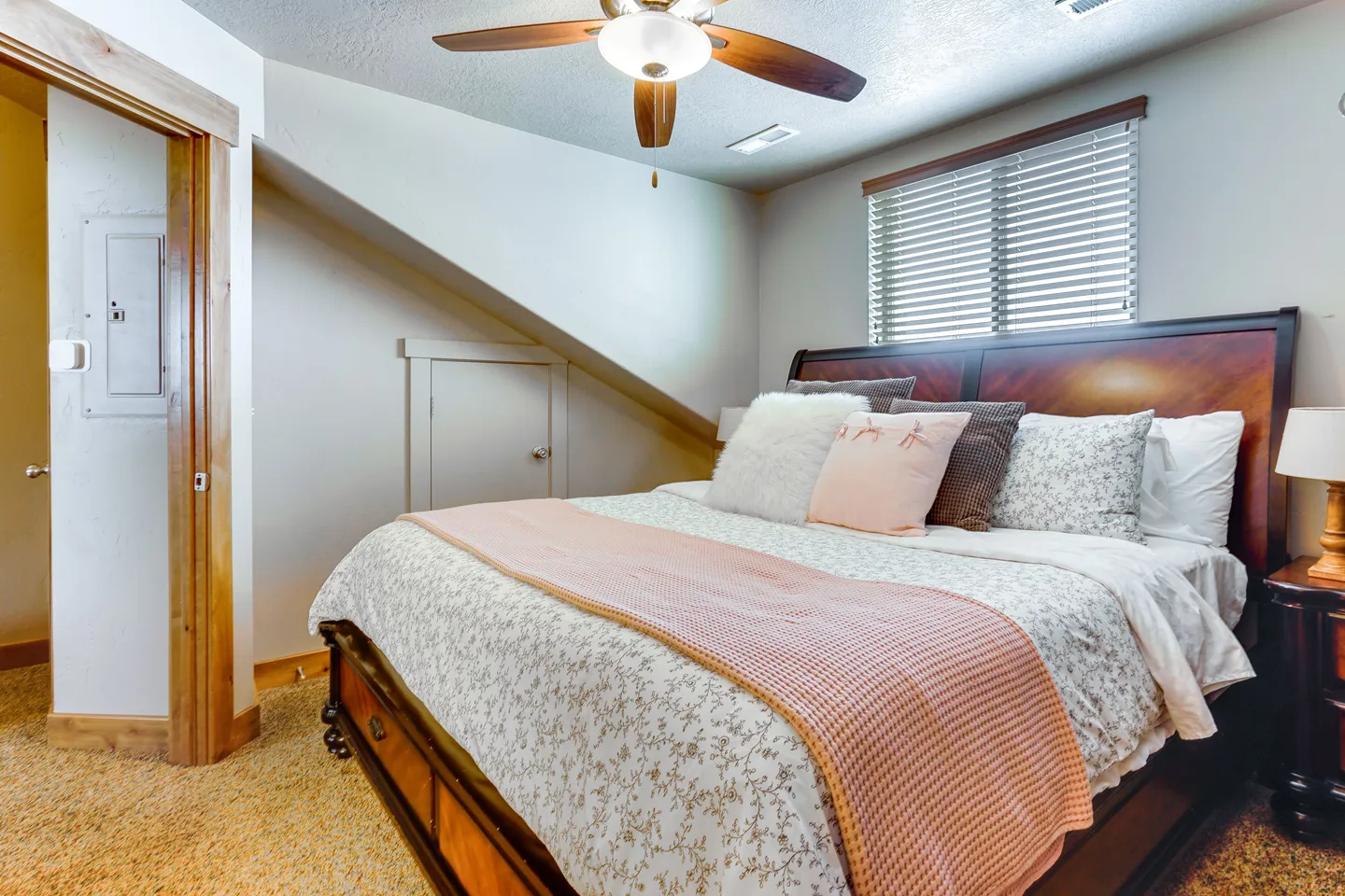 Bedroom featuring a made bed with a dark wood frame, angled ceiling, ceiling fan, and carpeted floor.