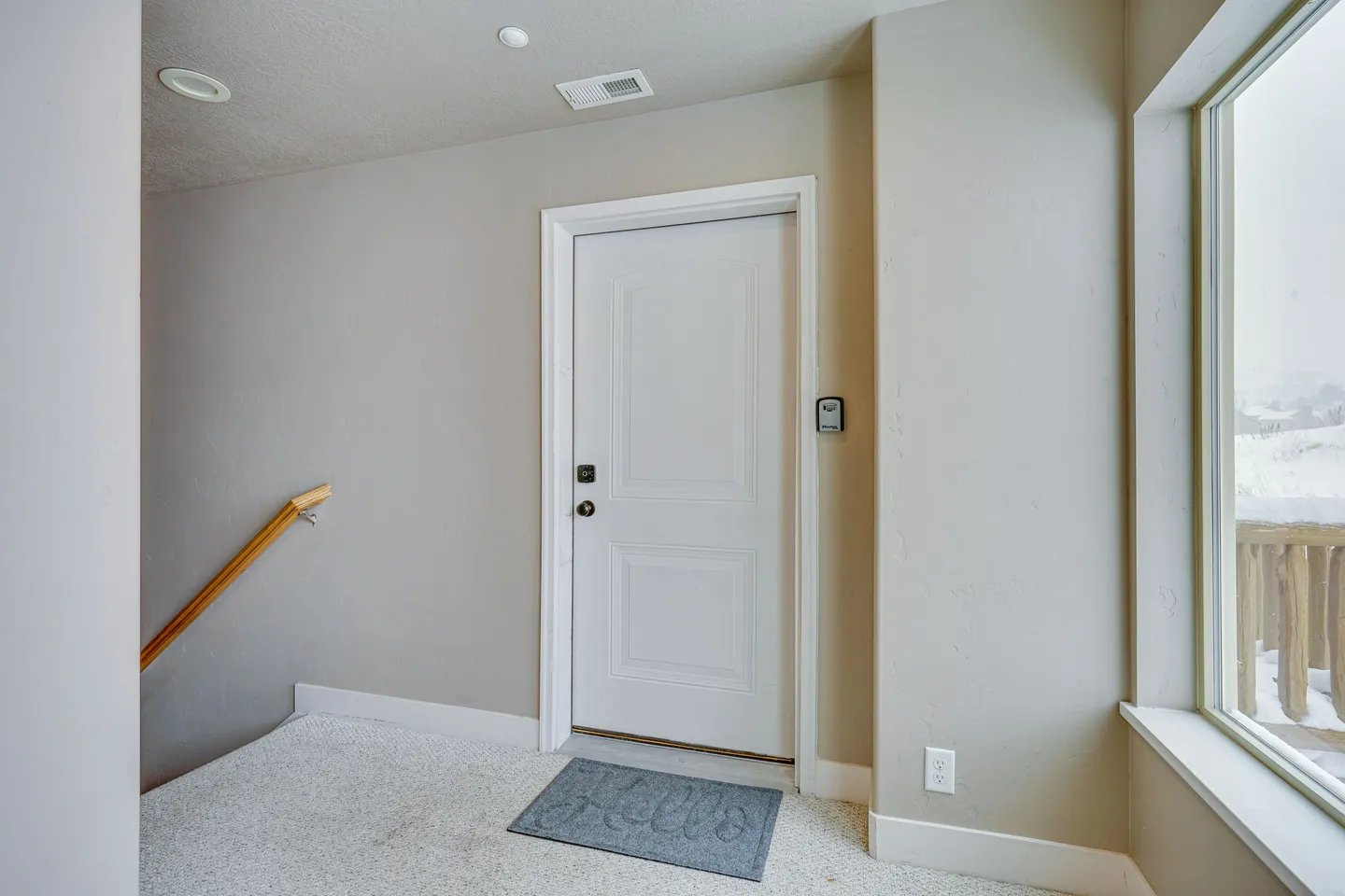 Front entryway with a white door, a gray welcome mat, carpeted flooring, and a large window looking out at a snowy exterior.