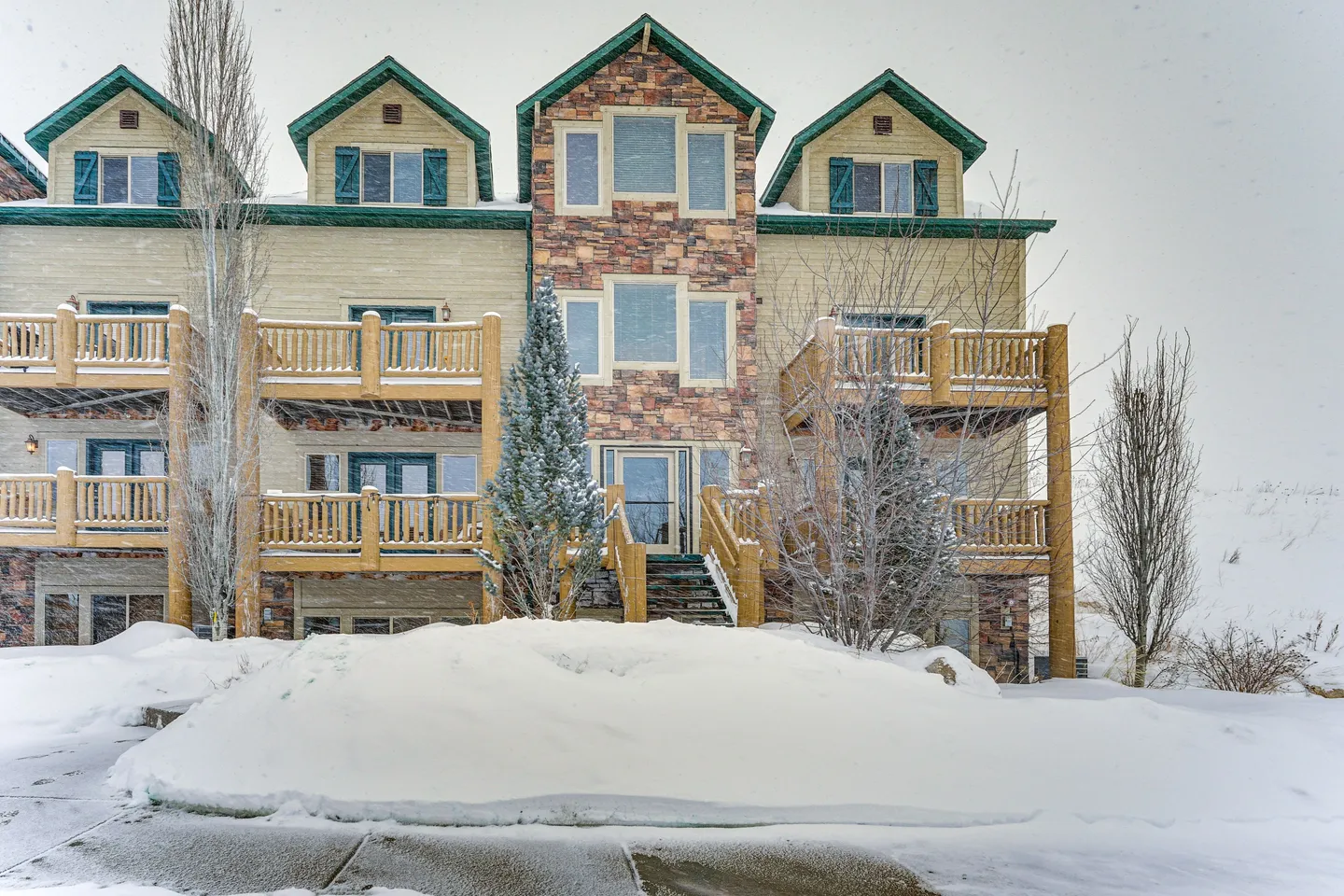 Exterior view of a multi-story lodge-style townhome building with stone accent and wooden balconies in winter with heavy snow.