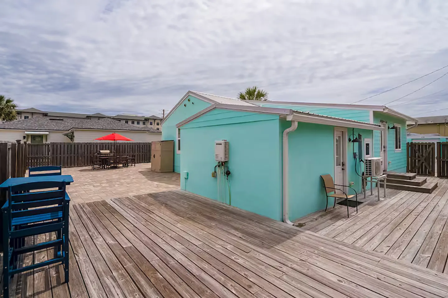Fenced backyard featuring a large weathered wood deck and a paved patio area behind a bright turquoise house.
