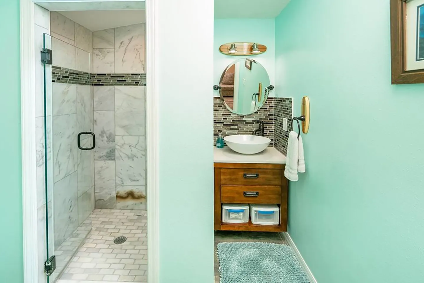 Bathroom with light teal walls, a walk-in tiled shower with a glass door, and a wood vanity with a vessel sink.