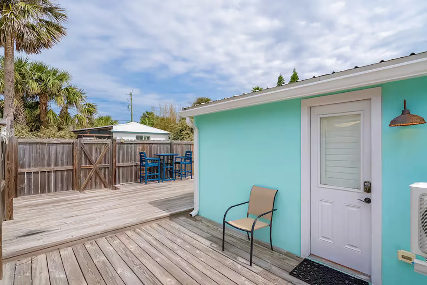 Multi-level wooden deck outside a turquoise house with patio seating and a wooden fence.
