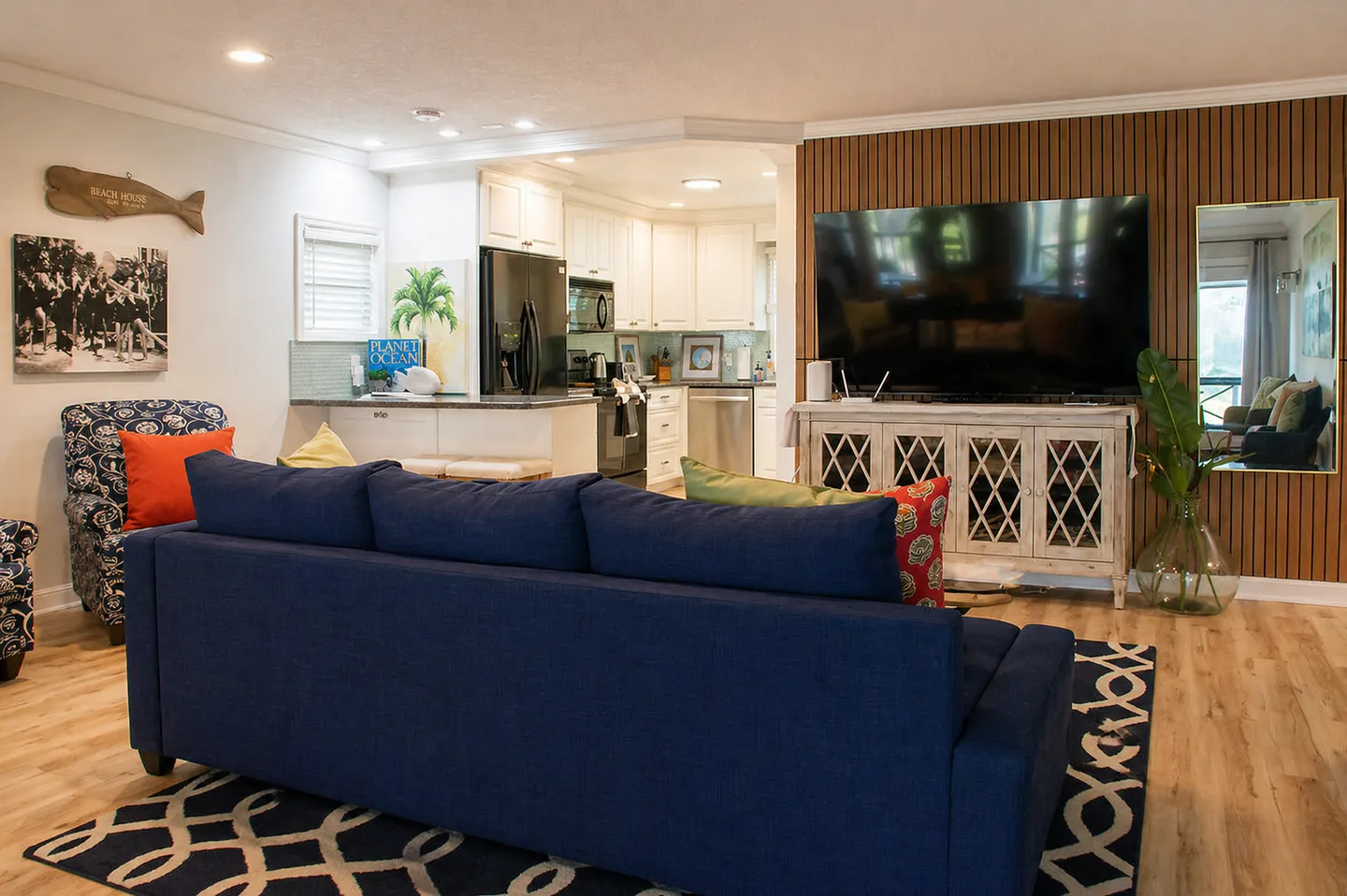 Open-concept living room with a blue sofa facing a large television and an open kitchen in the background.