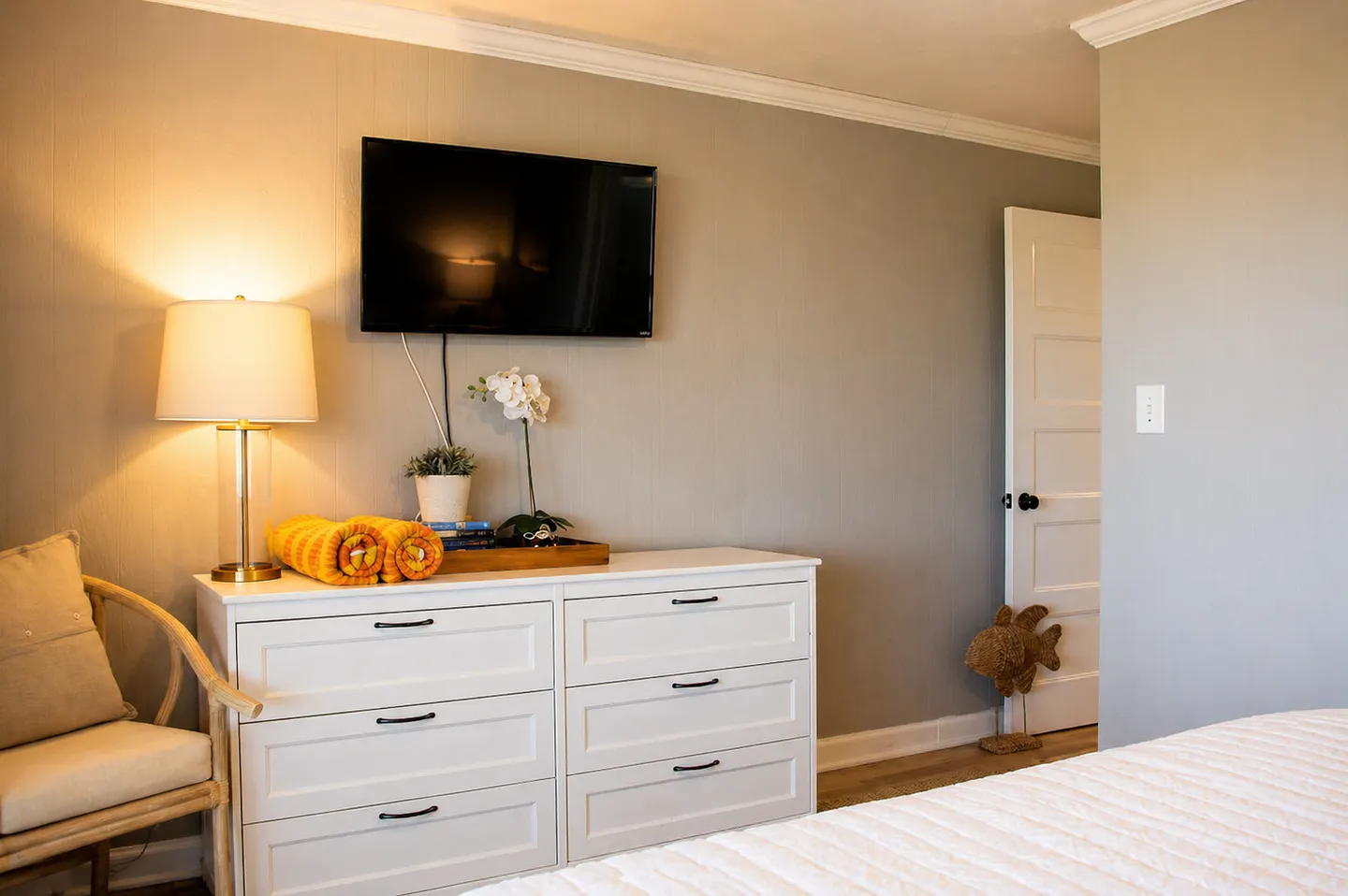 Bedroom featuring a white six-drawer dresser under a wall-mounted flat-screen TV, an armchair, and the foot of a bed.