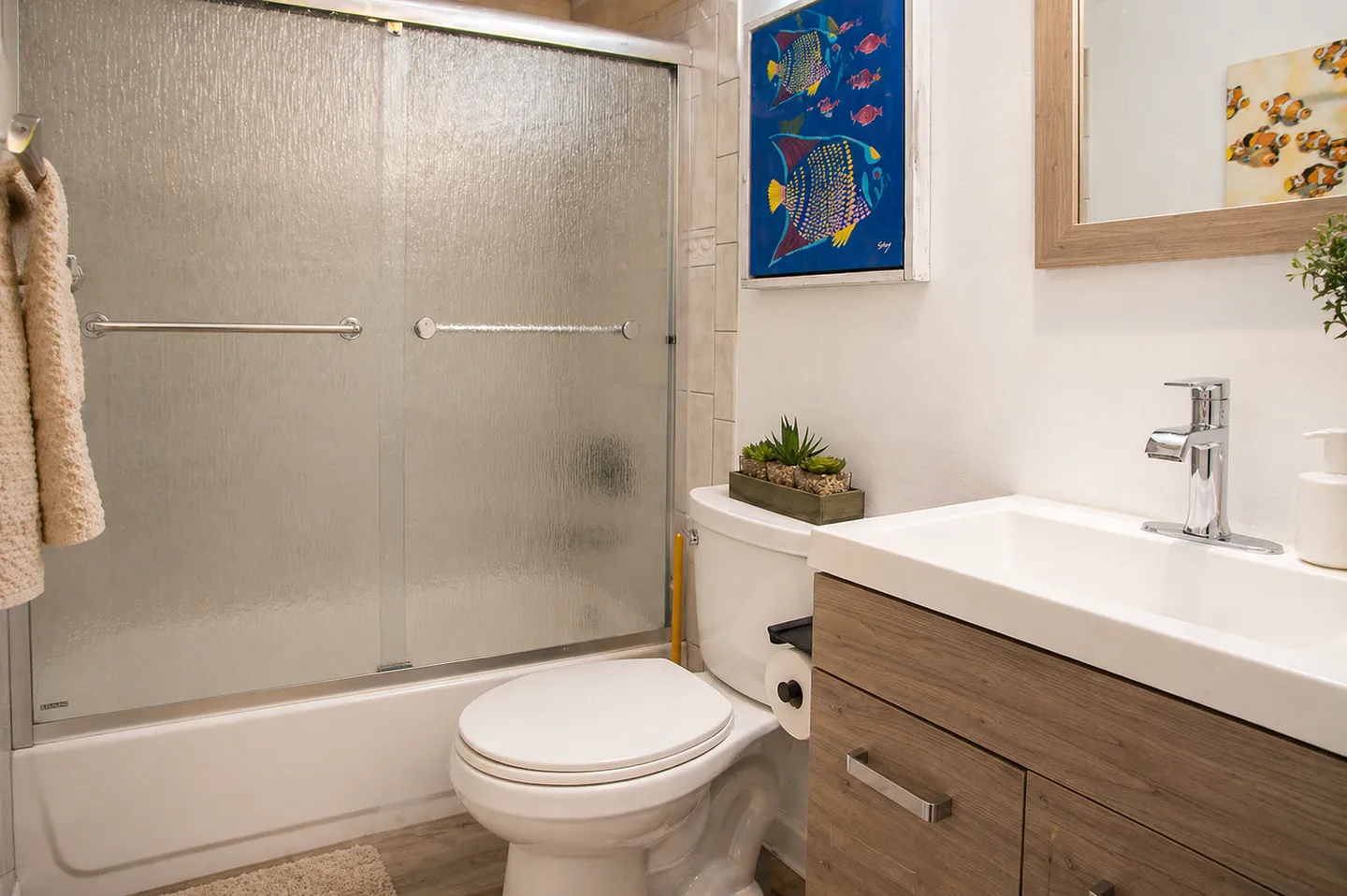 Bathroom with a textured glass sliding shower door over a tub, white toilet, and wooden vanity with a modern sink.