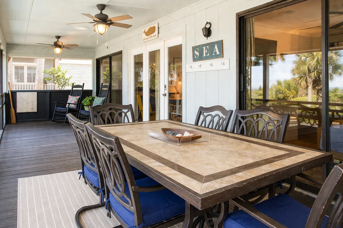 Screened porch with an outdoor dining table and chairs, ceiling fans, and rocking chairs in the background.