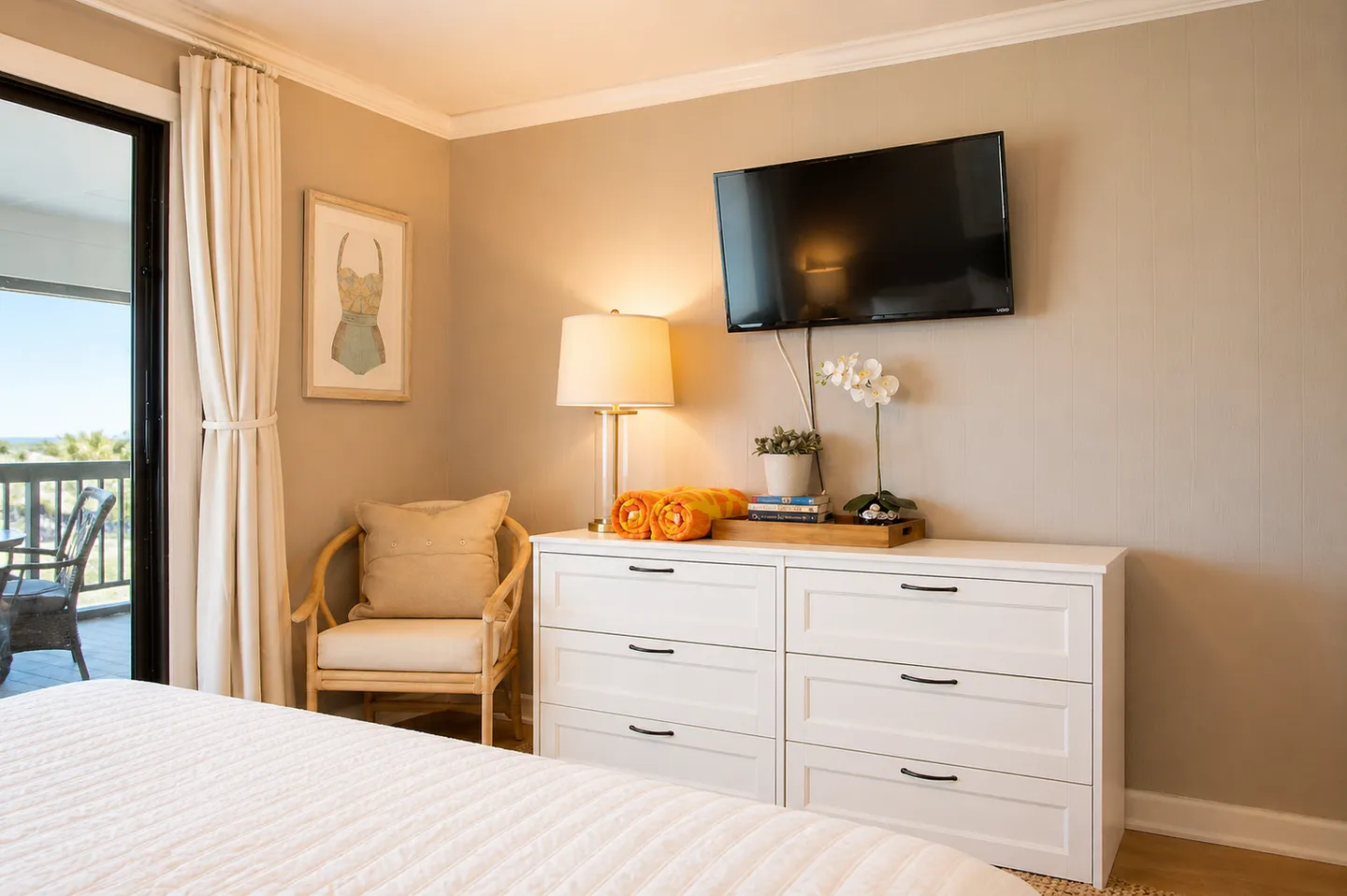 Bedroom featuring a white six-drawer dresser with a mounted television above, an accent armchair, and sliding glass doors leading to an outdoor deck.