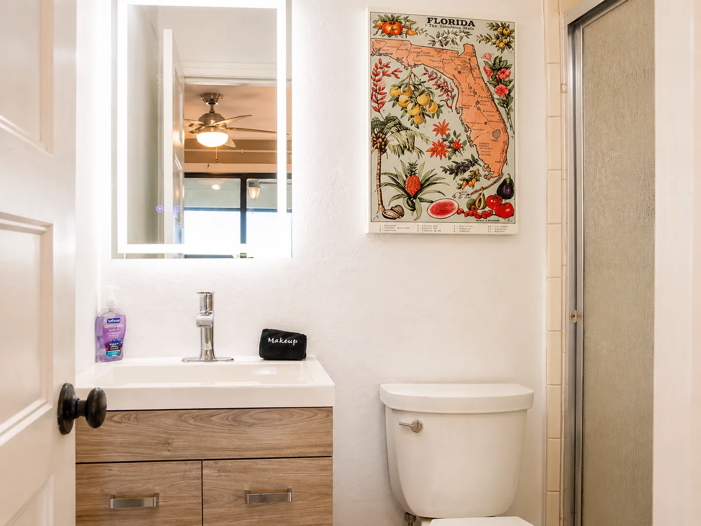 Bathroom with a wood-grain vanity, backlit mirror, toilet, and vintage Florida map art.