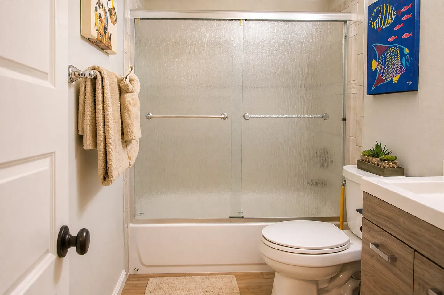Bathroom featuring a bathtub and shower combination with frosted sliding glass doors, a white toilet, and a vanity next to it.