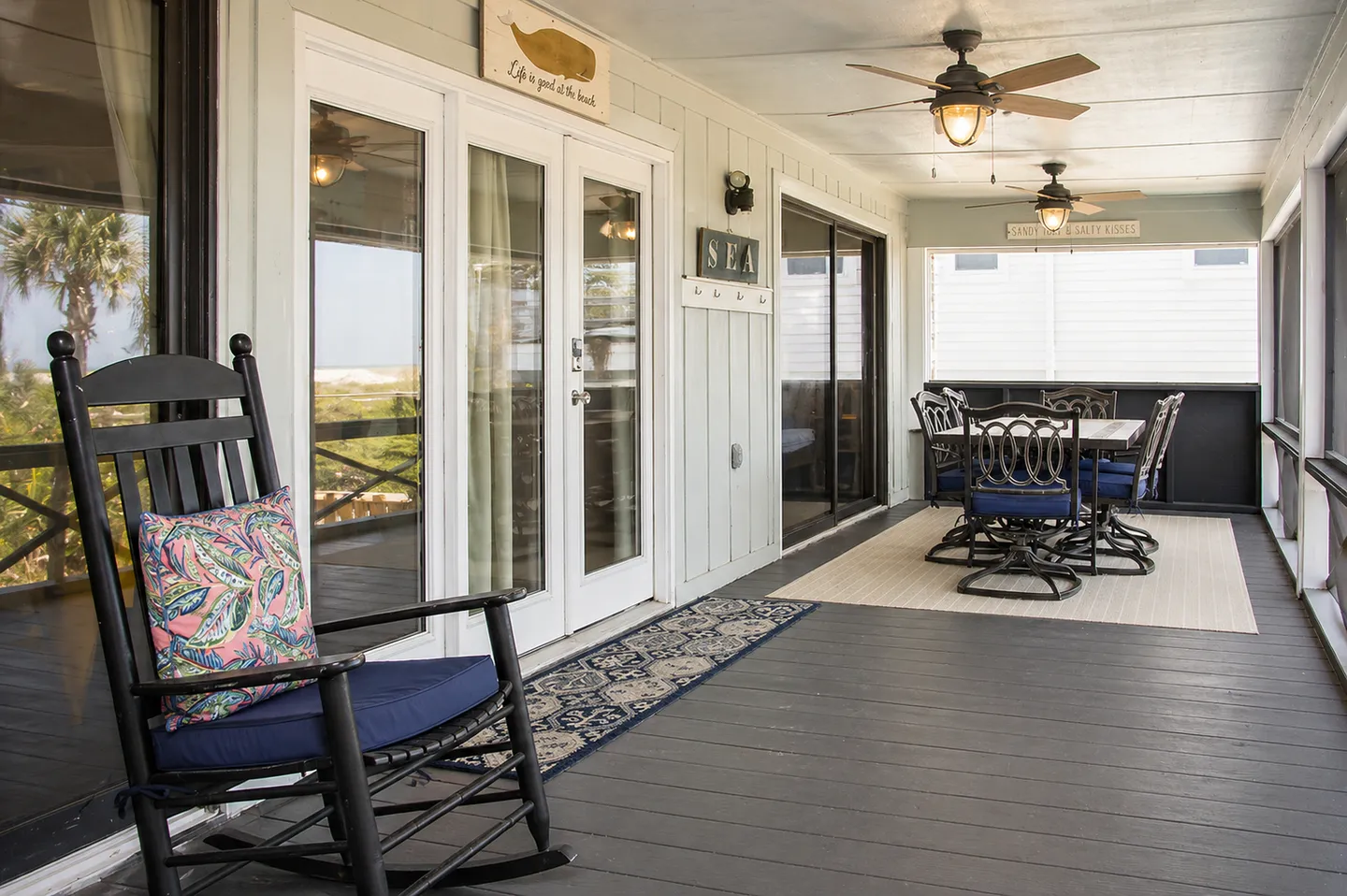 Screened porch with a rocking chair in the foreground and a dining table with chairs in the background.