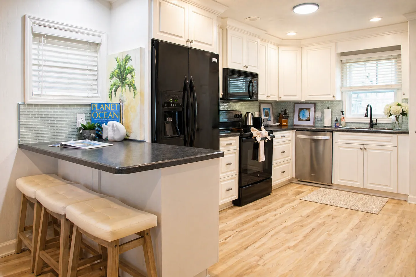 Kitchen with white cabinetry, dark countertops, a breakfast bar with three stools, and stainless steel and black appliances.