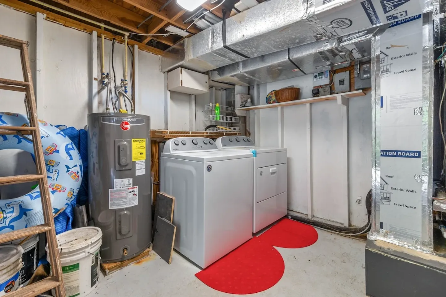 A basement utility area featuring a white washing machine and dryer next to a tall water heater, with exposed ductwork and joists above.