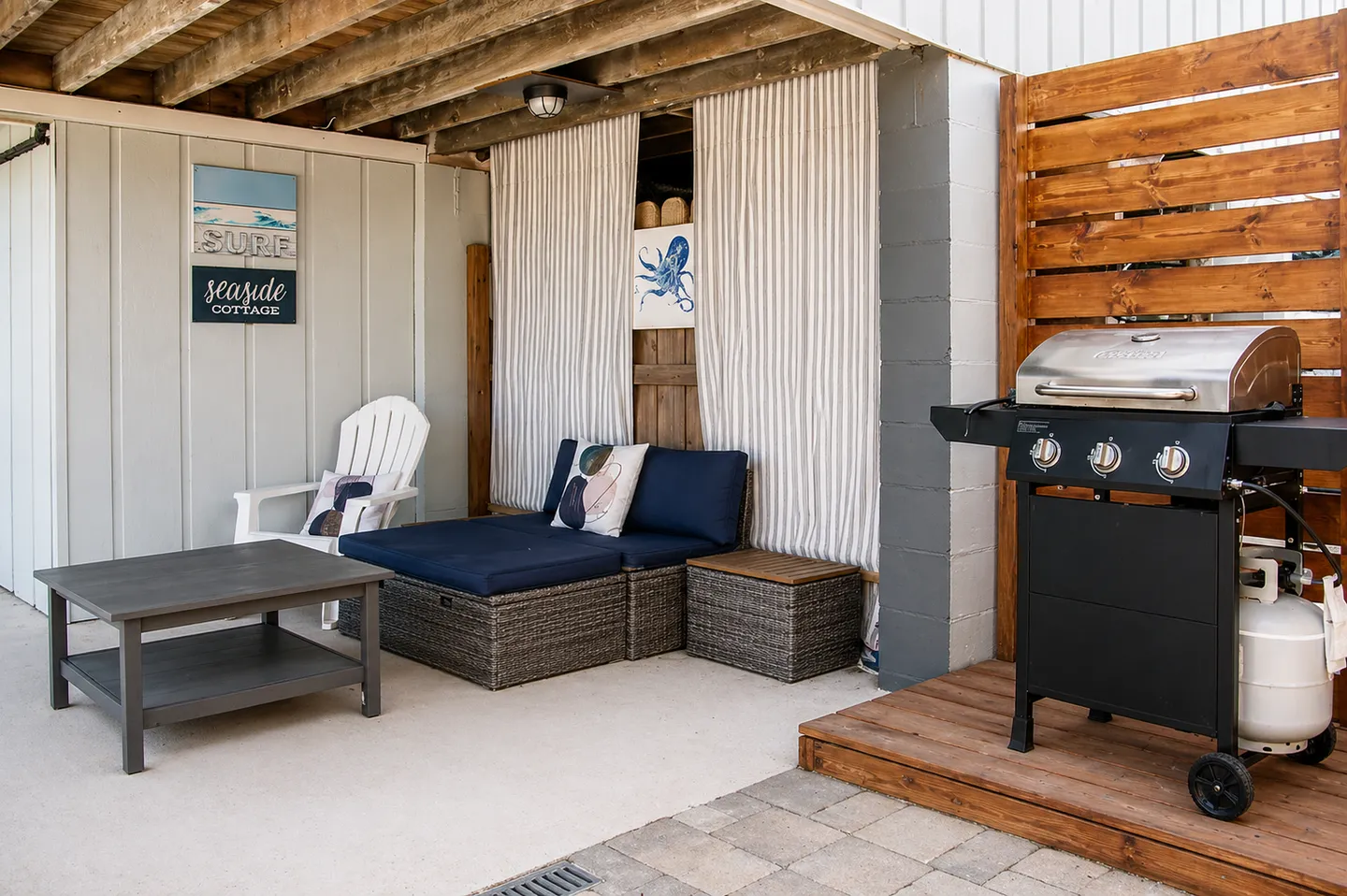 Covered outdoor patio with a wicker daybed, coffee table, white chair, and a gas grill.