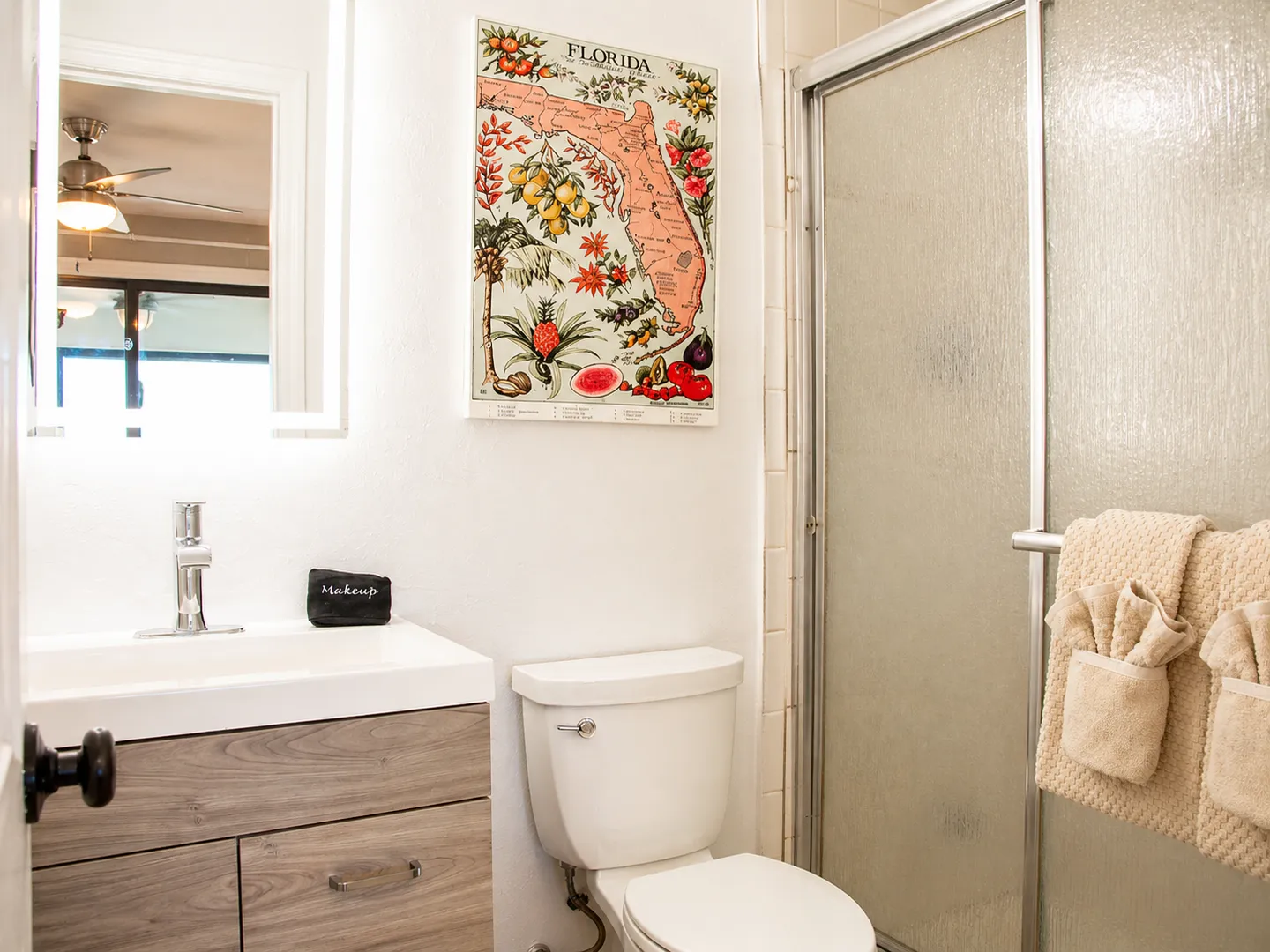 Bathroom with a wood-toned vanity, toilet, Florida map wall art, and frosted glass shower doors.
