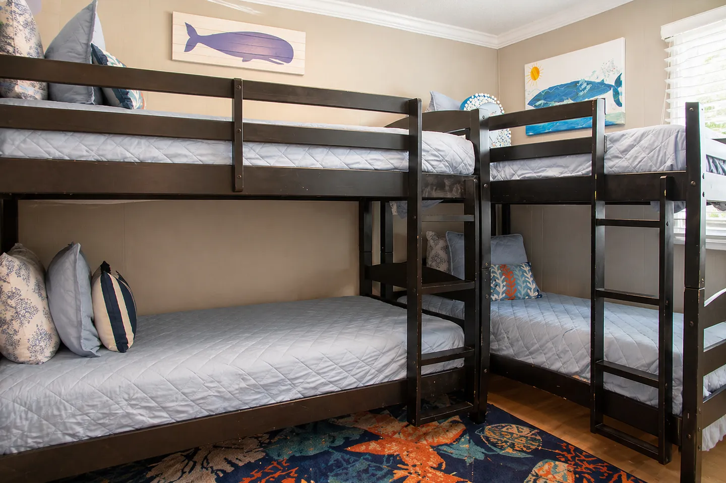 Bunk room with dark wooden L-shaped bunk beds, light blue quilted bedding, and whale wall art.